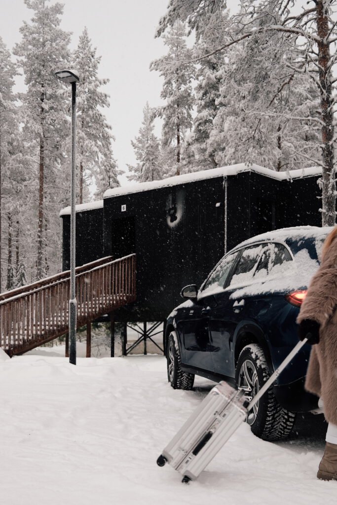 Guest with luggage arriving by car at a snowy NOA Villas cabin in Lapland.